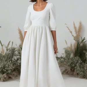 May include: A white, long-sleeved,  wedding dress with a scoop neckline and a gathered skirt.