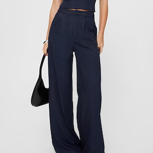 May include: Wide-leg pants in a navy blue pinstripe pattern. The pants have a high waist and a relaxed fit.