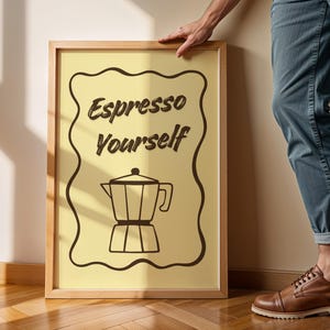 Può includere: Una stampa incorniciata con sfondo giallo chiaro e bordo ondulato marrone. Il testo "Espresso Yourself" è sopra un disegno a tratto di una caffettiera. La cornice è in legno marrone chiaro.