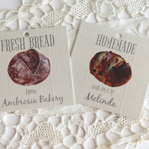 May include: Two brown paper gift tags with images of loaves of bread. The tag on the left says "FRESH BREAD from Ambrosia Bakery". The tag on the right says "HOMEMADE with love by Melinda".