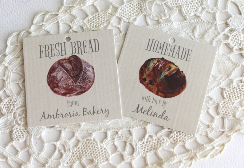 May include: Two brown paper gift tags with images of loaves of bread. The tag on the left says "FRESH BREAD from Ambrosia Bakery". The tag on the right says "HOMEMADE with love by Melinda".