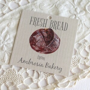 May include: A brown and white gift tag with the text "FRESH BREAD from Ambrosia Bakery". A drawing of a loaf of bread is in the center of the tag.