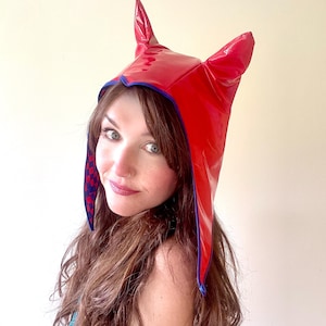 May include: A red hooded hat with devil horns, trimmed in blue. The hat is made of a shiny, possibly vinyl material.