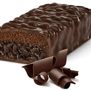 May include: A chocolate-covered brownie bar with a layer of chocolate chips. The bar is broken in half, revealing the inside. Chocolate curls are scattered around the bar.