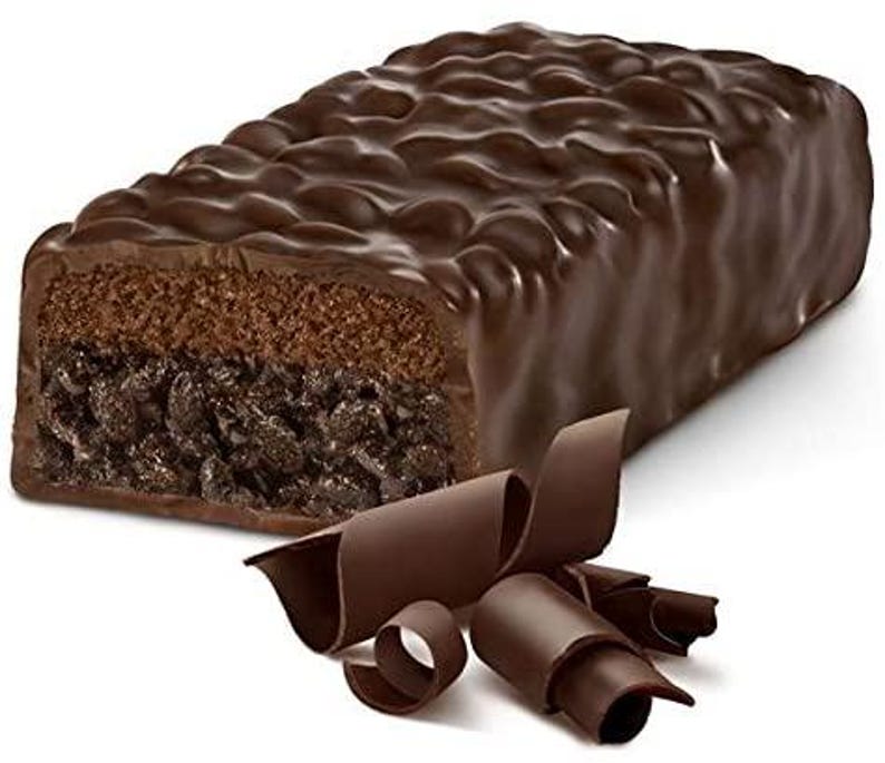 May include: A chocolate-covered brownie bar with a layer of chocolate chips. The bar is broken in half, revealing the inside. Chocolate curls are scattered around the bar.