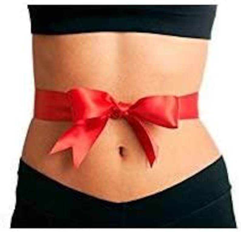 May include: A woman's torso with a red satin ribbon tied around her waist in a bow.