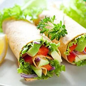 May include: Two vegetarian wraps filled with lettuce, avocado, red pepper, and onion. The wraps are on a white plate with a lemon wedge.