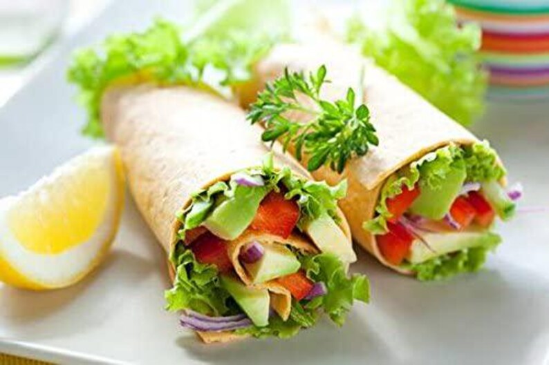 May include: Two vegetarian wraps filled with lettuce, avocado, red pepper, and onion. The wraps are on a white plate with a lemon wedge.
