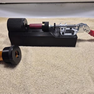 Peut inclure: Un outil de gabarit en plastique noir doté d'une bride de serrage métallique avec une poignée rouge, un composant cylindrique moleté et un insert bordeaux. Une pièce détachée séparée se compose d'un cylindre métallique doré fixé à un capuchon moleté noir.
