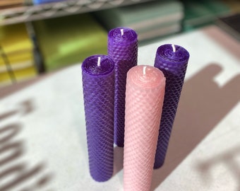 May include: Four candles, three purple and one pink, are arranged in a row. The candles are made of honeycomb wax and have a textured surface.