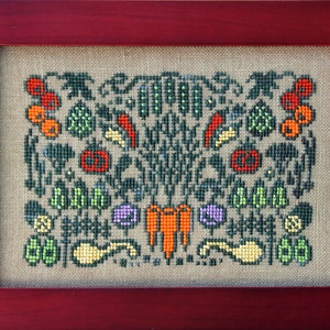 May include: A cross-stitch embroidery design featuring a variety of vegetables, including carrots, peas, peppers, and tomatoes. The design is framed in a dark red wood frame.