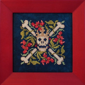 Puede incluir: Arte de punto de cruz que representa una calavera coronada, rodeada de flores rojas, hojas verdes y huesos cruzados. La obra está enmarcada en un marco cuadrado rojo. El fondo es de tela azul oscuro.