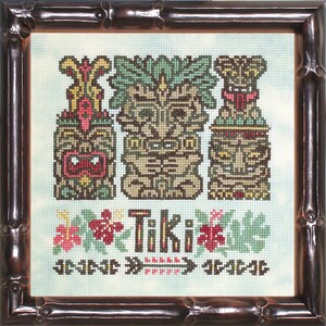 Peut inclure: Broderie au point de croix représentant trois figures Tiki marron, vertes et rouges, sur fond bleu clair. Le mot "Tiki" est brodé en dessous, avec des motifs floraux et de flèches. L'œuvre est encadrée dans un cadre en bambou brun foncé.