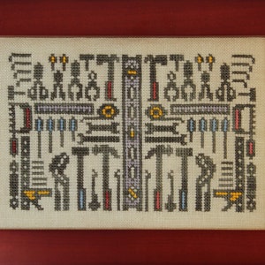 May include: A cross-stitch embroidery design featuring a variety of tools, including hammers, wrenches, and screwdrivers. The tools are arranged in a symmetrical pattern, with a central column of tools and two flanking columns. The embroidery is done in a variety of colours, including black, white, red, blue, and yellow.