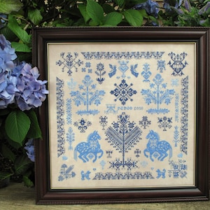 May include: A framed cross-stitch embroidery featuring a blue and white floral design with stylised trees, horses, and geometric patterns. The embroidery is titled "NINO 2010".