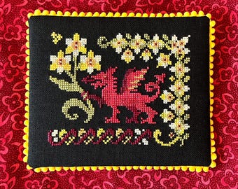 May include: A black and yellow embroidered pillow with a red dragon and yellow flowers. The pillow has a black background and a yellow border.