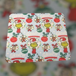 May include: A light blue rectangular mousepad featuring a repeating pattern of the Grinch in a Santa hat, Cindy Lou Who, Max the dog, and Christmas ornaments. The words "GRINCH" and "NAUGHTY MICE" are also visible.