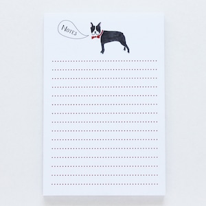 May include: A white notepad with a black and white illustration of a Boston Terrier wearing a red bow tie. The notepad has the word "NOTES" written in a speech bubble above the dog. The notepad has red dotted lines.