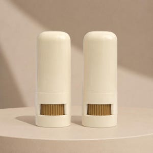 May include: Two cylindrical off-white containers with rounded tops. Each container features a horizontal cutout near the base, revealing a textured, brownish-gold ribbed component inside. The design is smooth, minimalist, and uniform in appearance.