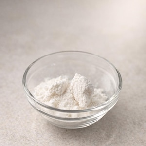 Könnte beinhalten: Eine klare Glasschüssel gefüllt mit weißem Pulver, möglicherweise Mehl. Die Schüssel ist rund mit leicht ausgestelltem Rand und steht auf einer neutralen Oberfläche. Das Pulver ist in der Mitte der Schüssel angehäuft.