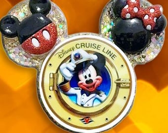 May include: A Disney Cruise Line badge reel featuring a circular porthole design with Mickey Mouse in a captain's uniform. The top has glittery Mickey and Minnie ears. Below the porthole are three beads: one white with gold spots, one white, and one gold.