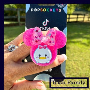 May include: A pink PopSockets phone grip featuring a Minnie Mouse design with a bow and a Tsum Tsum character. The grip has a glittery finish and the TikTok logo is visible on the packaging. The words "Irish Family" are at the bottom.