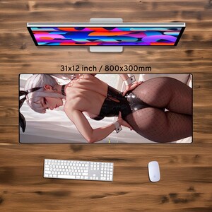 May include: A large rectangular desk mat featuring a detailed illustration of a woman in a black outfit. The mat is 31x12 inches (79x30 cm) and includes a keyboard, mouse, and a computer monitor.