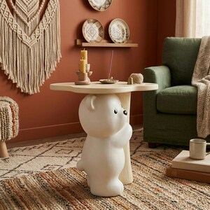 May include: A whimsical, off-white side table featuring a bear-shaped base supporting a light-colored, tree-shaped tabletop. The table is placed on a patterned rug, with a green armchair and decorative items in the background. The table is approximately 24 inches tall.