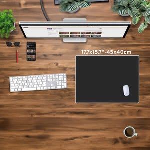 May include: A black rectangular mouse pad, measuring 17.7 x 15.7 inches, with a white border and a white mouse. The pad is on a wooden desk, along with a keyboard, monitor, and a cup of coffee.