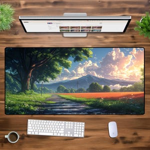 Op de afbeelding: Een grote rechthoekige bureaumat met een landschap van een weg, bomen en een berg onder een blauwe lucht met wolken. Een computermonitor, toetsenbord en muis liggen op een houten bureau.
