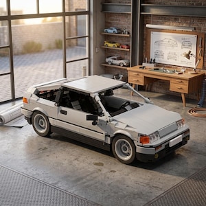 May include: A white and black model car, constructed from interlocking blocks, sits in a garage setting. The car has a detailed design with visible wheels, headlights, and a removable roof. The garage features a desk, blueprints, and other model cars.