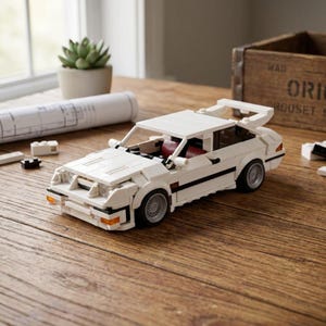 May include: A white toy car with black accents, a rear spoiler, and silver wheels. The car has red interior details and is constructed from interlocking blocks. The car is on a wooden surface.