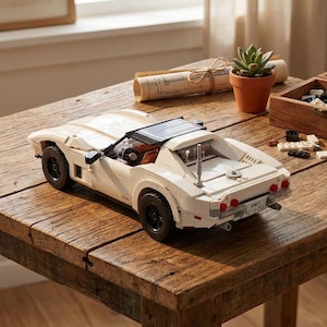 May include: A white Lego model car with black wheels and a black roof. The car is on a wooden table. The car has a license plate that reads "82-10-295".