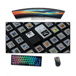May include: A black and gray gaming mousepad with a variety of retro video game cartridges printed on it. The mousepad is next to a black and gray keyboard with rainbow colored keys and a black and gray gaming mouse.