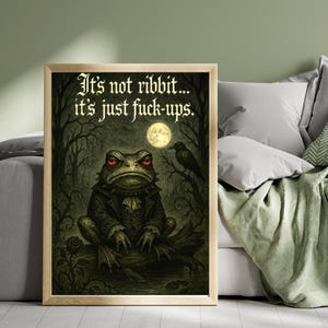 May include: Framed art print with a gothic illustration of a frog in a suit, red-eyed, under a full moon. The text reads, "It's not ribbit... it's just fuck-ups."