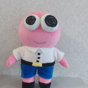 Puede incluir: Un juguete de peluche rosa con grandes ojos blancos y pupilas negras. El juguete lleva una camisa blanca con botones negros, pantalones azules y un cinturón amarillo.