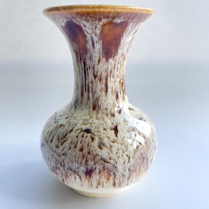 May include: A small, ceramic vase with a bulbous base and flared rim. The vase features a speckled pattern of brown and cream colors, with a glossy finish. The rim is a solid brown. This decorative vase is suitable for displaying flowers or as a standalone accent piece.