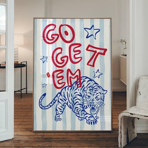 May include: A framed art print featuring a blue and white striped background with the words "GO GET 'EM" in red. A blue and white tiger illustration is at the bottom. The artwork is displayed in a room with a wooden floor.