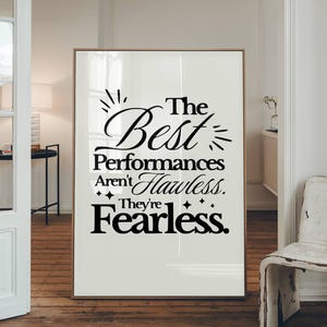 Puede incluir: Una impresión artística enmarcada con el texto "The Best Performances Aren't Flawless. They're Fearless." El texto negro se muestra sobre un fondo blanco, enmarcado en un marco dorado. La impresión se muestra en una habitación con pisos de madera.