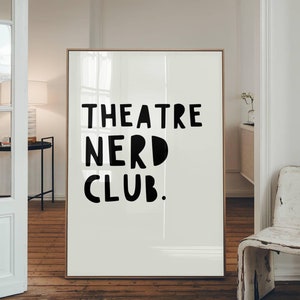 May include: A white poster with black text that reads "THEATRE NERD CLUB." The poster is hanging on a wall in a room with white walls and wooden floors.