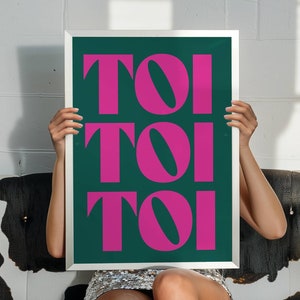 May include: A framed print with the word "TOI" repeated three times in a bold, pink font on a dark green background.