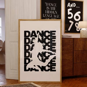 Puede incluir: Una impresión artística enmarcada con la palabra "DANCE" apilada verticalmente, con una silueta de bailarina blanca. Se ven dos impresiones enmarcadas más pequeñas con texto. El texto de las impresiones más pequeñas dice "DANCE IS THE HIDDEN LANGUAGE" y "AND... 56 78".