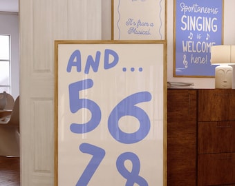 May include: Three framed art prints with text. The largest print has the words "AND... 56 78" in blue on a white background. Two smaller prints read "It's from a Musical" and "Spontaneous SINGING is WELCOME & here!" in blue.