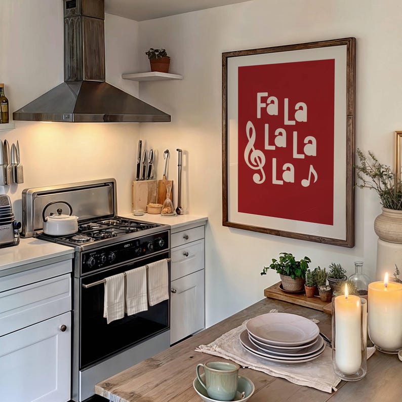 May include: A framed print with a red background and white text that reads "Fa La La La La" with a treble clef and a musical note. The print is hanging on a white wall in a kitchen.