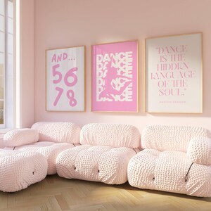 May include: A light pink living room with three framed art prints and a modular sofa. The art includes the text "AND... 56 78", a dancer silhouette, and the quote "DANCE IS THE HIDDEN LANGUAGE OF THE SOUL". The sofa is a light pink, textured fabric.