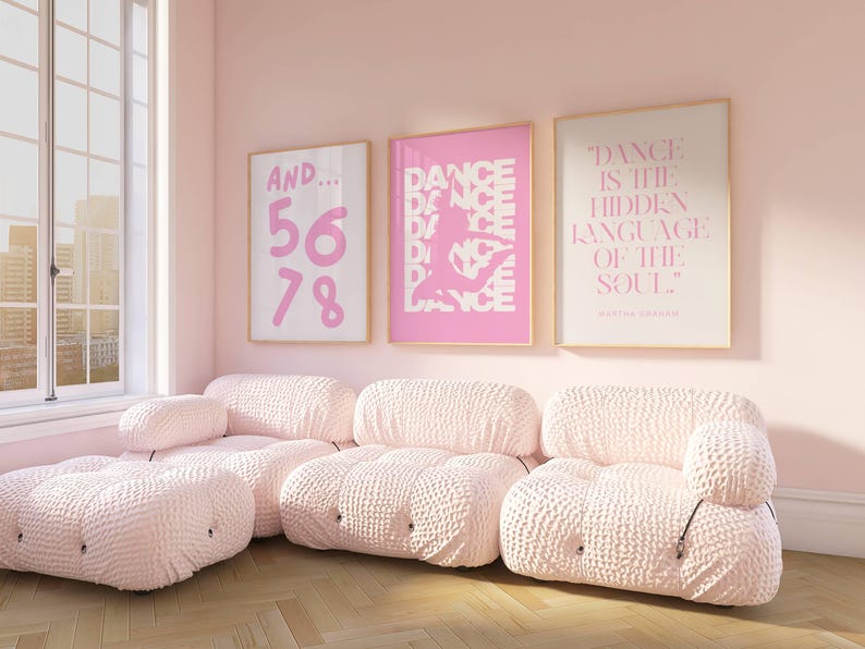 May include: A light pink living room with three framed art prints and a modular sofa. The art includes the text "AND... 56 78", a dancer silhouette, and the quote "DANCE IS THE HIDDEN LANGUAGE OF THE SOUL". The sofa is a light pink, textured fabric.