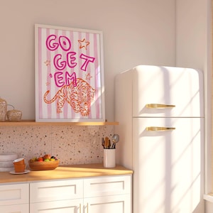 K&ouml;nnte beinhalten: Ein gerahmter Kunstdruck mit den Worten "GO GET 'EM" in Pink und Orange sowie einer Tigerillustration. Das Kunstwerk ist vor einem gestreiften Hintergrund platziert. Der Druck wird in einer K&uuml;chenumgebung angezeigt.