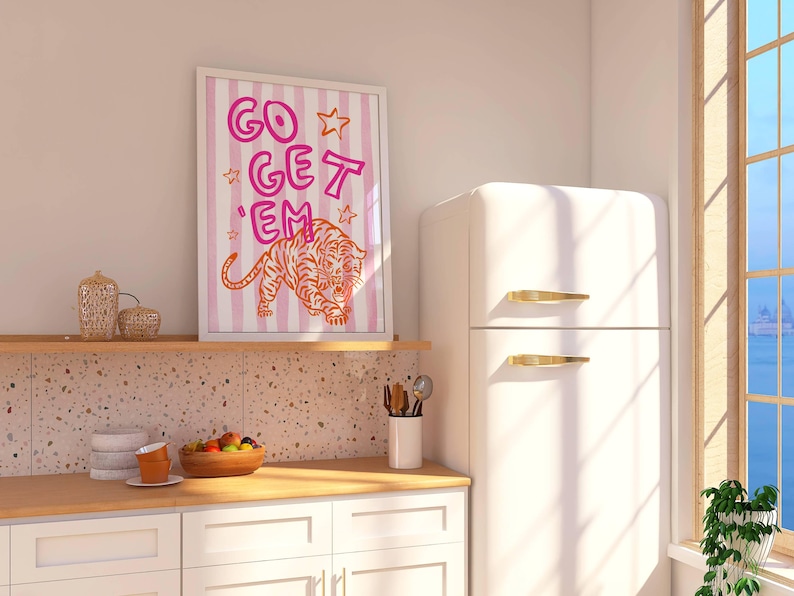K&ouml;nnte beinhalten: Ein gerahmter Kunstdruck mit den Worten "GO GET 'EM" in Pink und Orange sowie einer Tigerillustration. Das Kunstwerk ist vor einem gestreiften Hintergrund platziert. Der Druck wird in einer K&uuml;chenumgebung angezeigt.