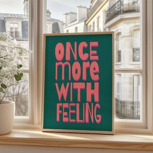 May include: A teal framed print with the text "ONCE MORE WITH FEELING" in pink lettering.