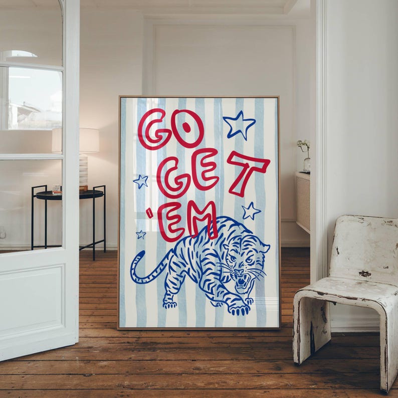 May include: A framed art print featuring a blue and white striped background with the words "GO GET 'EM" in red. A blue and white tiger illustration is at the bottom. The artwork is displayed in a room with a wooden floor.